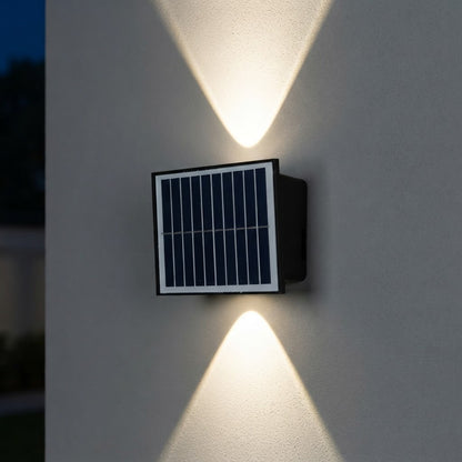 Lámpara solar de pared encendida de noche, proyectando un haz de luz hacia arriba y otro hacia abajo sobre la pared
